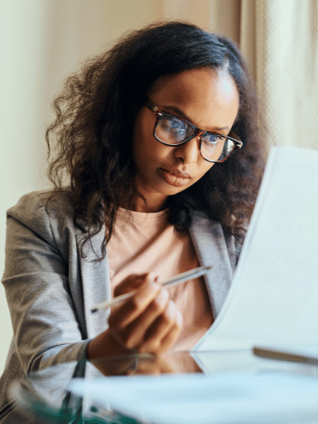 black woman with glasses and wearing coral shirt with grey dress jacket, looking at paperwork