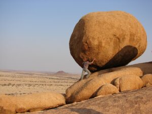 Man looking like he's pushing a massive boulder uphill.