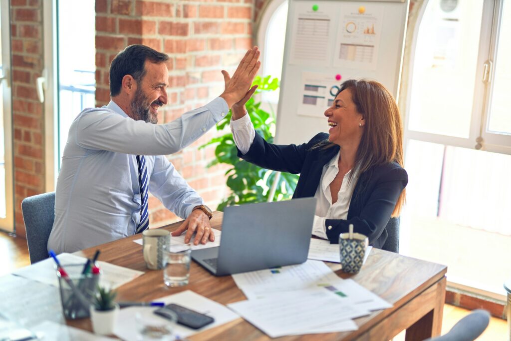 A man and a woman high-fiving each other while sitting at a table with a laptop open in front of them.